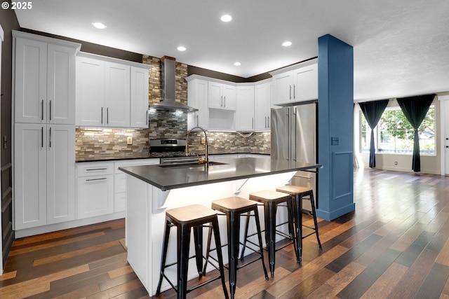 5416 Wales Dr, Eugene, OR 97402 - kitchen featuring wall chimney exhaust hood, dark countertops, appliances with stainless steel finishes, a kitchen breakfast bar, and dark wood finished floors