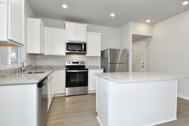 kitchen with a kitchen island, white cabinets, light stone counters, light hardwood / wood-style floors, and stainless steel appliances