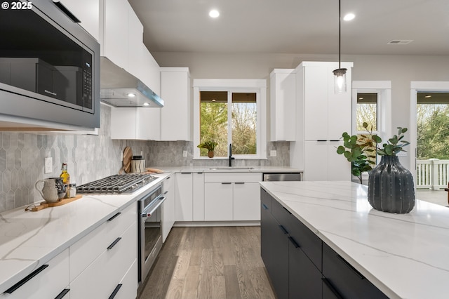 kitchen with appliances with stainless steel finishes, decorative light fixtures, sink, white cabinets, and wall chimney range hood