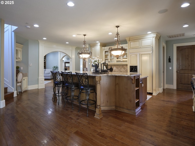 kitchen featuring pendant lighting, decorative backsplash, a large island, light stone counters, and cream cabinetry