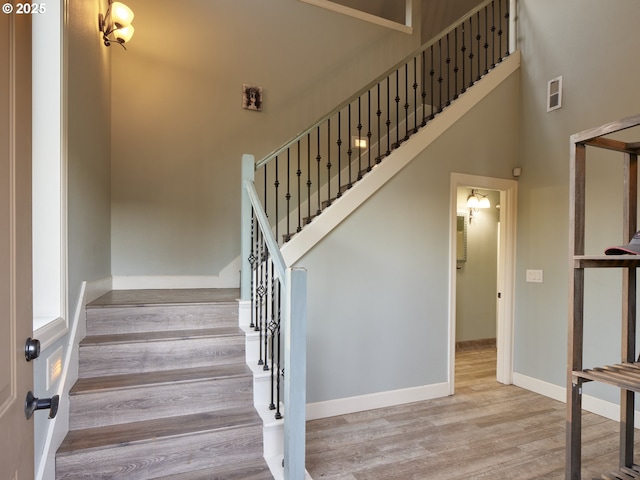 staircase with wood-type flooring and a towering ceiling