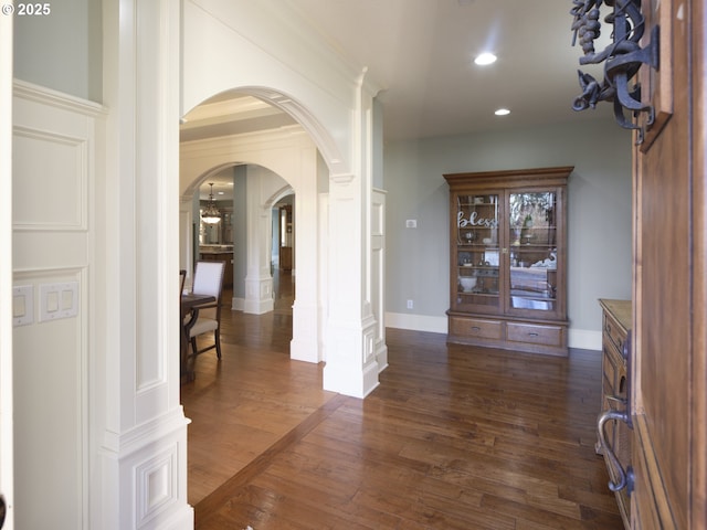 hall with ornate columns, ornamental molding, and dark wood-type flooring