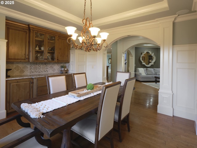 dining space with a notable chandelier, a tray ceiling, dark wood-type flooring, and ornamental molding