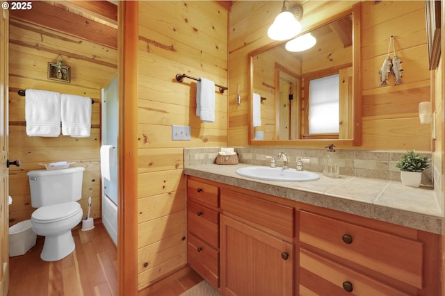 bathroom featuring wooden walls, toilet, wood finished floors, and vanity