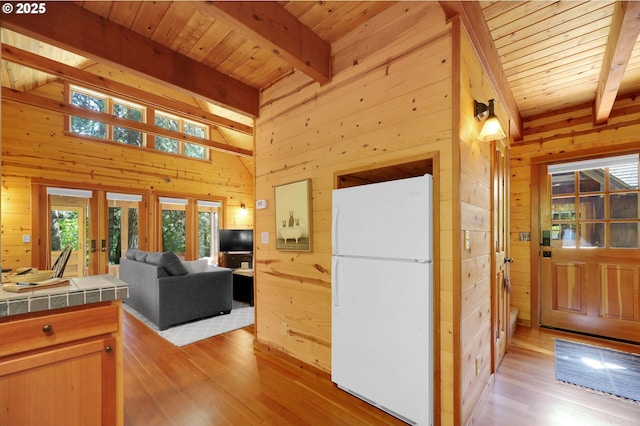 kitchen with freestanding refrigerator, tile countertops, beam ceiling, and wooden walls