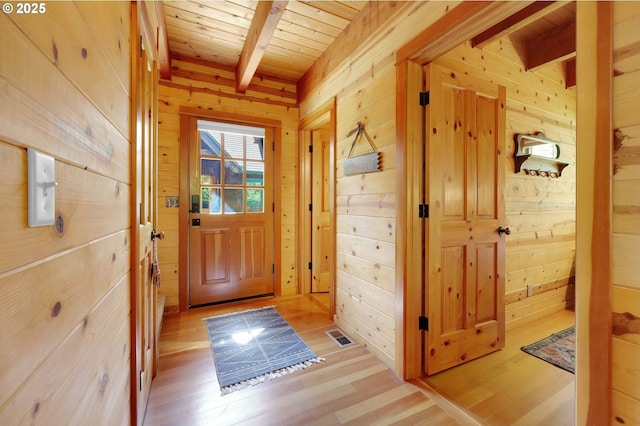 doorway with wooden walls, beam ceiling, light wood-style floors, wooden ceiling, and visible vents