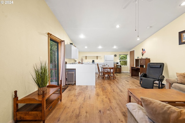 living room featuring radiator heating unit, vaulted ceiling, and light wood-type flooring