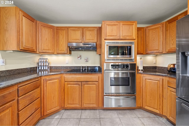 kitchen featuring stainless steel appliances, light tile patterned floors, and dark stone counters