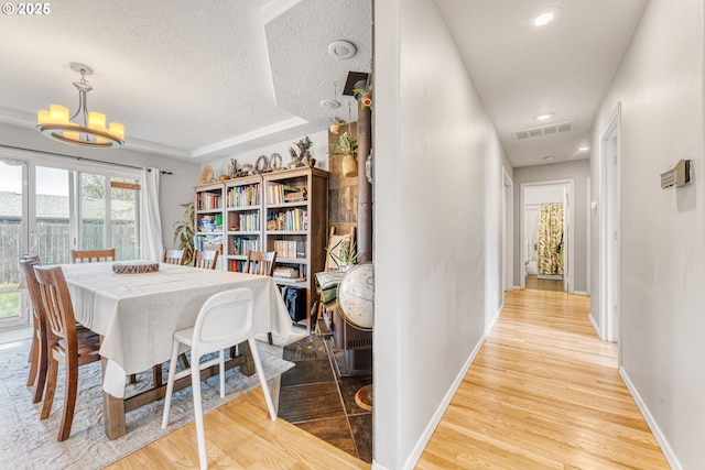 dining room featuring an inviting chandelier, a textured ceiling, light hardwood / wood-style floors, and a tray ceiling