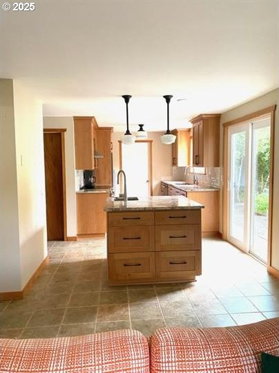 4315 High St, Eugene, OR 97405 - kitchen featuring backsplash, light tile patterned floors, a kitchen island with sink, decorative light fixtures, and brown cabinets