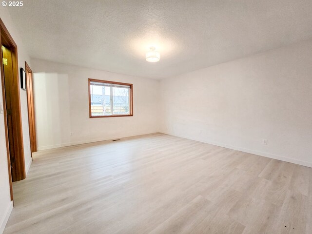 unfurnished room with a textured ceiling, light wood-type flooring, visible vents, and baseboards