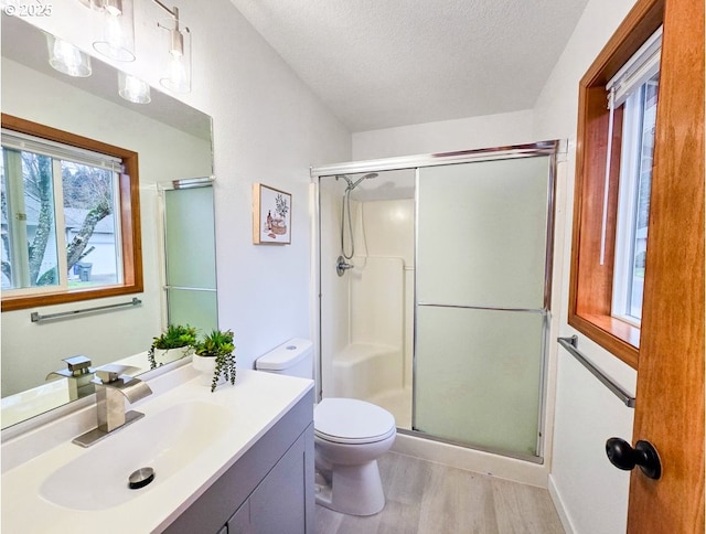 bathroom with toilet, a stall shower, vanity, a textured ceiling, and wood finished floors