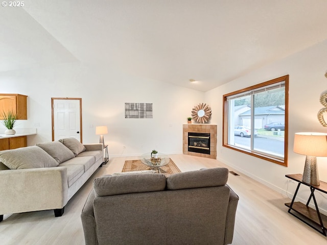 living room with high vaulted ceiling, light wood-style flooring, visible vents, baseboards, and a tiled fireplace