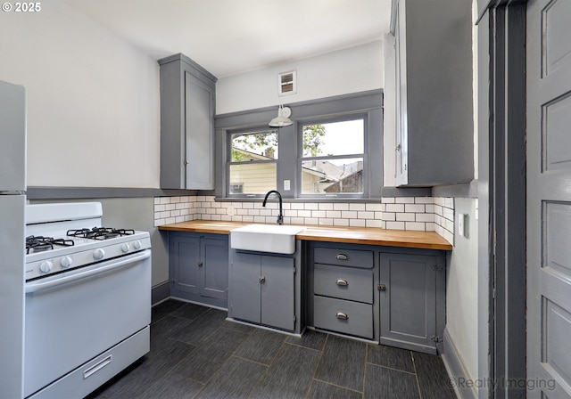 kitchen with wood counters, white appliances, gray cabinetry, a sink, and tasteful backsplash
