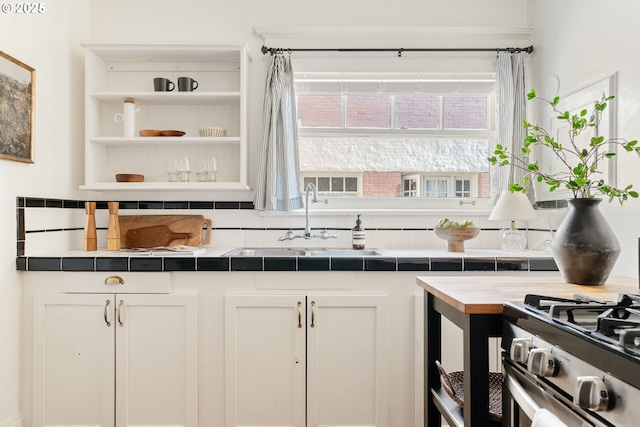 kitchen featuring white cabinetry, tile counters, stainless steel range with gas stovetop, and sink