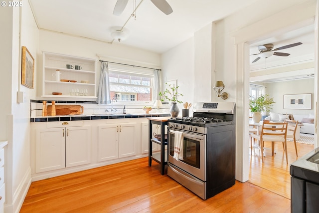 kitchen with white cabinets, tile counters, ceiling fan, stainless steel range with gas stovetop, and light wood-type flooring