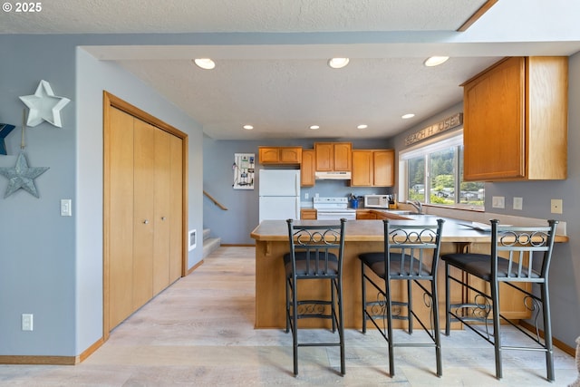 33645 Resort Dr, Pacific City, OR 97135 - kitchen featuring white appliances, under cabinet range hood, a peninsula, a textured ceiling, and brown cabinetry