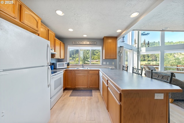 33645 Resort Dr, Pacific City, OR 97135 - kitchen with white appliances, a textured ceiling, a peninsula, recessed lighting, and light wood-style flooring