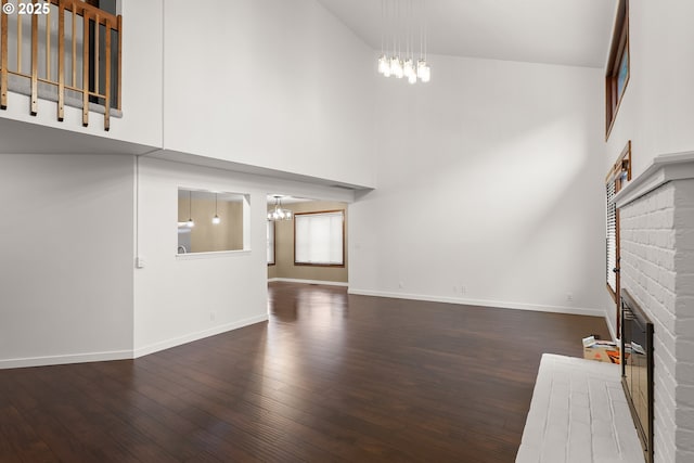 unfurnished living room featuring wood finished floors, baseboards, a fireplace, a towering ceiling, and a chandelier