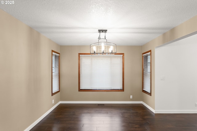 unfurnished dining area featuring an inviting chandelier, baseboards, dark wood-style flooring, and a textured ceiling