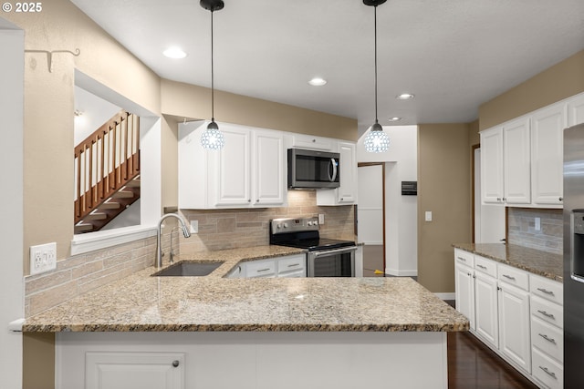 kitchen featuring light stone counters, appliances with stainless steel finishes, a peninsula, white cabinets, and a sink