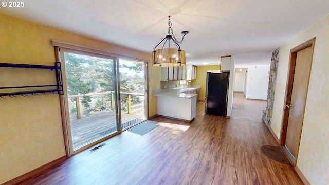 kitchen featuring wood finished floors, visible vents, a peninsula, freestanding refrigerator, and light countertops