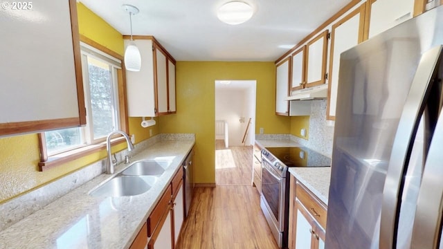 kitchen with under cabinet range hood, decorative light fixtures, appliances with stainless steel finishes, light wood-style floors, and a sink