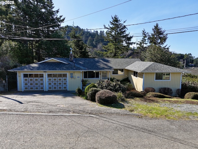 single story home featuring an attached garage, a chimney, driveway, and a shingled roof