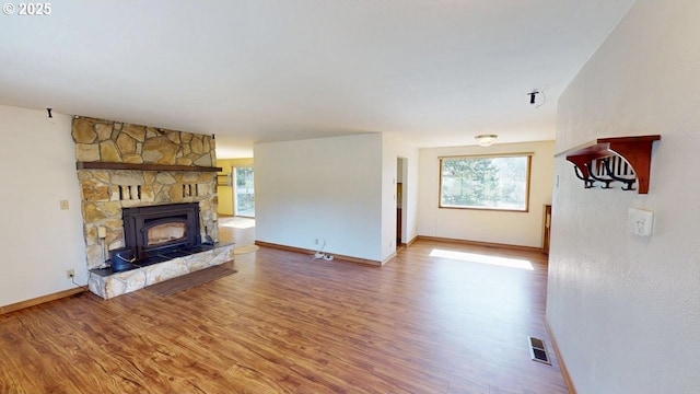 unfurnished living room with visible vents, baseboards, a stone fireplace, and wood finished floors