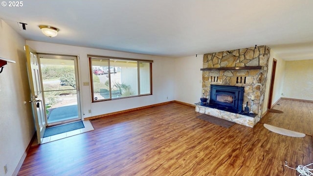 unfurnished living room with a stone fireplace, baseboards, and wood finished floors