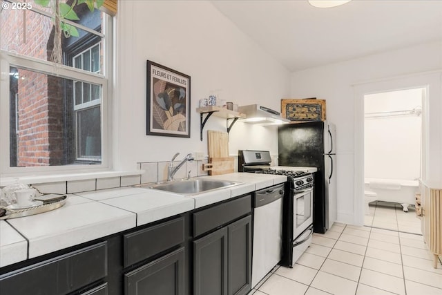 kitchen with sink, appliances with stainless steel finishes, extractor fan, tile counters, and light tile patterned flooring