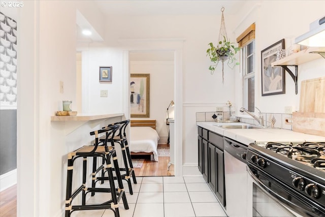 kitchen with dishwasher, sink, light tile patterned flooring, and gas range