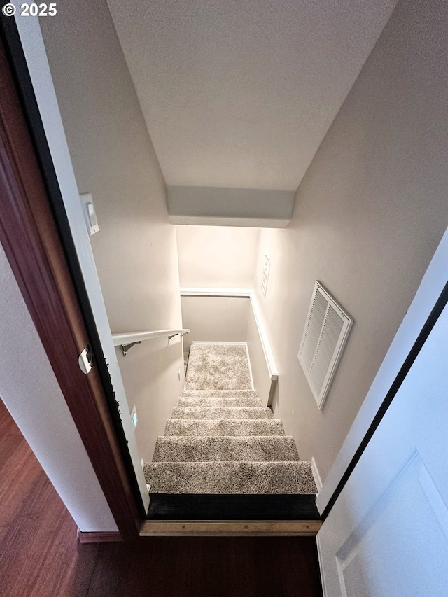 stairway featuring wood finished floors and visible vents