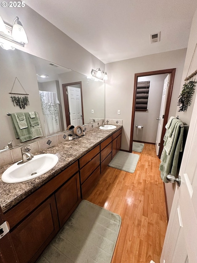 bathroom with a sink, visible vents, wood finished floors, and double vanity