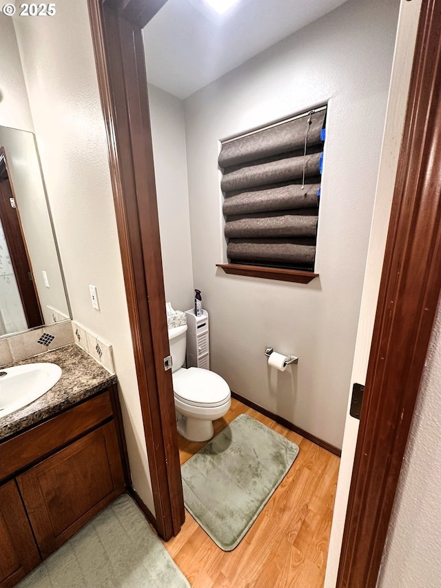 bathroom with toilet, vanity, baseboards, and wood finished floors