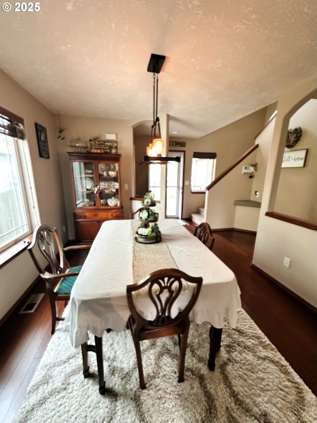 dining room featuring visible vents, baseboards, arched walkways, dark wood-style floors, and a textured ceiling