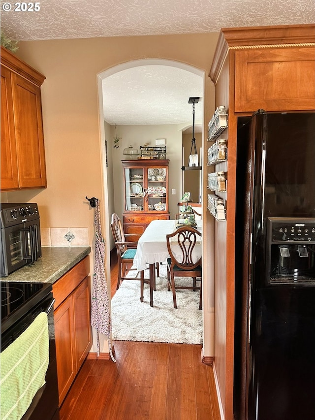 kitchen with brown cabinets, black appliances, a textured ceiling, dark wood finished floors, and arched walkways