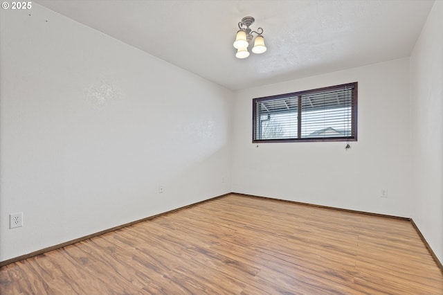 spare room with light wood-type flooring and a notable chandelier