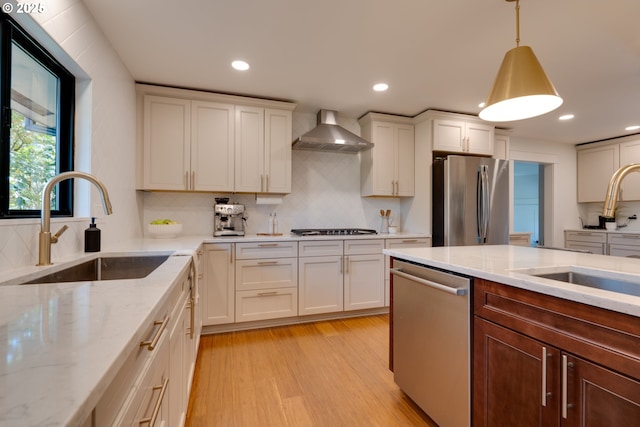 kitchen featuring stainless steel appliances, light stone countertops, sink, wall chimney range hood, and pendant lighting