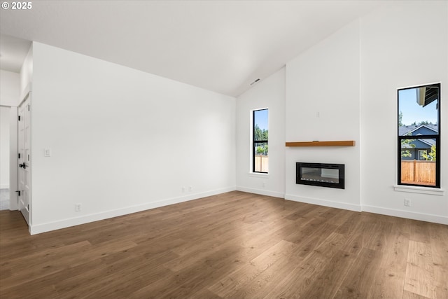 88109 Jameson Way, Veneta, OR 97487 - unfurnished living room featuring high vaulted ceiling, a glass covered fireplace, wood finished floors, and baseboards