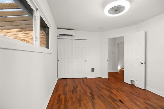 unfurnished bedroom with a closet, baseboards, wood finished floors, and a wall mounted air conditioner