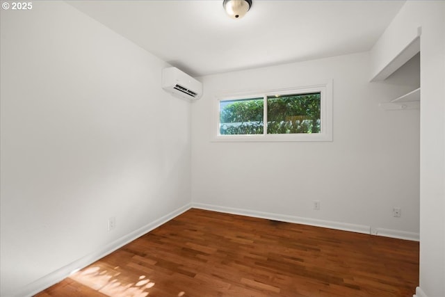 spare room with a wall unit AC, baseboards, and wood finished floors