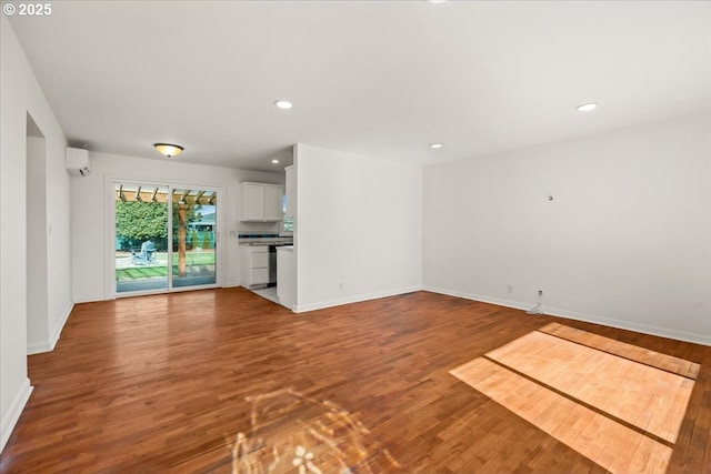 unfurnished living room featuring baseboards, an AC wall unit, wood finished floors, and recessed lighting