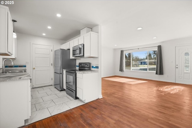 kitchen with light wood finished floors, stainless steel appliances, white cabinetry, a sink, and recessed lighting