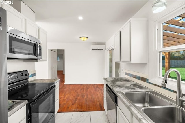 kitchen with a wall unit AC, stainless steel appliances, light wood-style floors, white cabinetry, and a sink