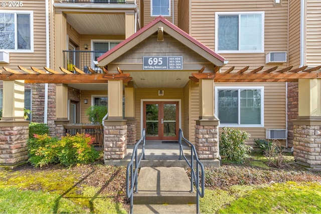 view of exterior entry with stone siding, french doors, and a pergola