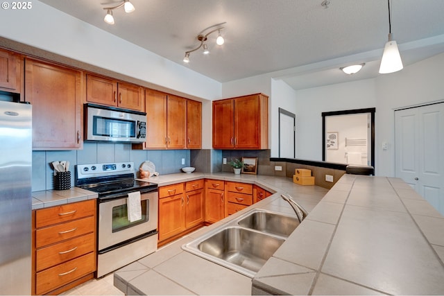 695 NW Falling Waters Ln Unit 304, Portland, OR 97229 - kitchen with stainless steel appliances, tile counters, a sink, a peninsula, and backsplash