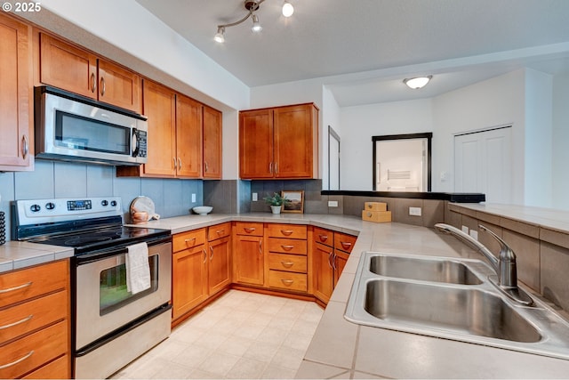 695 NW Falling Waters Ln Unit 304, Portland, OR 97229 - kitchen with stainless steel appliances, a sink, brown cabinets, backsplash, and a peninsula