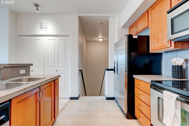 695 NW Falling Waters Ln Unit 304, Portland, OR 97229 - kitchen with appliances with stainless steel finishes, a sink, decorative backsplash, light countertops, and brown cabinetry