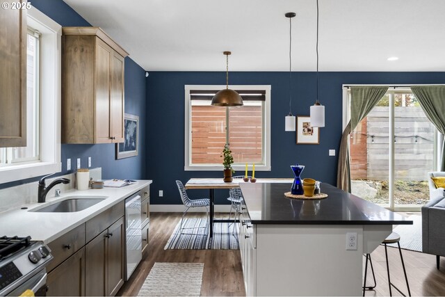 kitchen with appliances with stainless steel finishes, a sink, baseboards, a kitchen bar, and dark wood-style floors